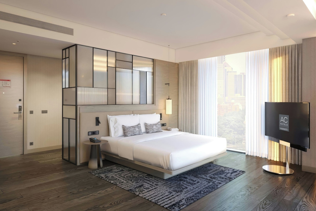 A modern hotel room with a large bed, a TV, and a city view.