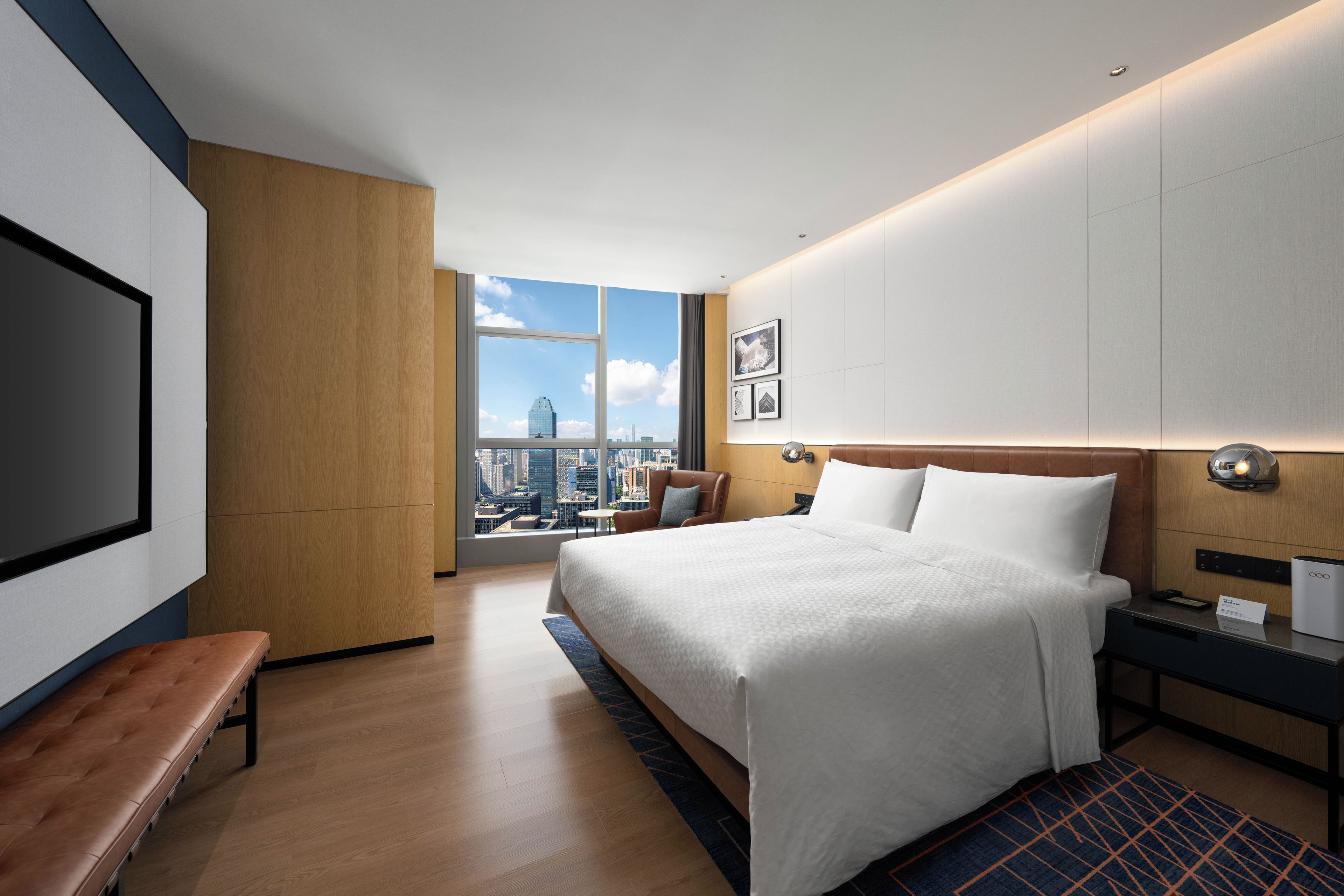 Quarto de hotel moderno com uma cama grande, uma escrivaninha, um banco e vista para a cidade.