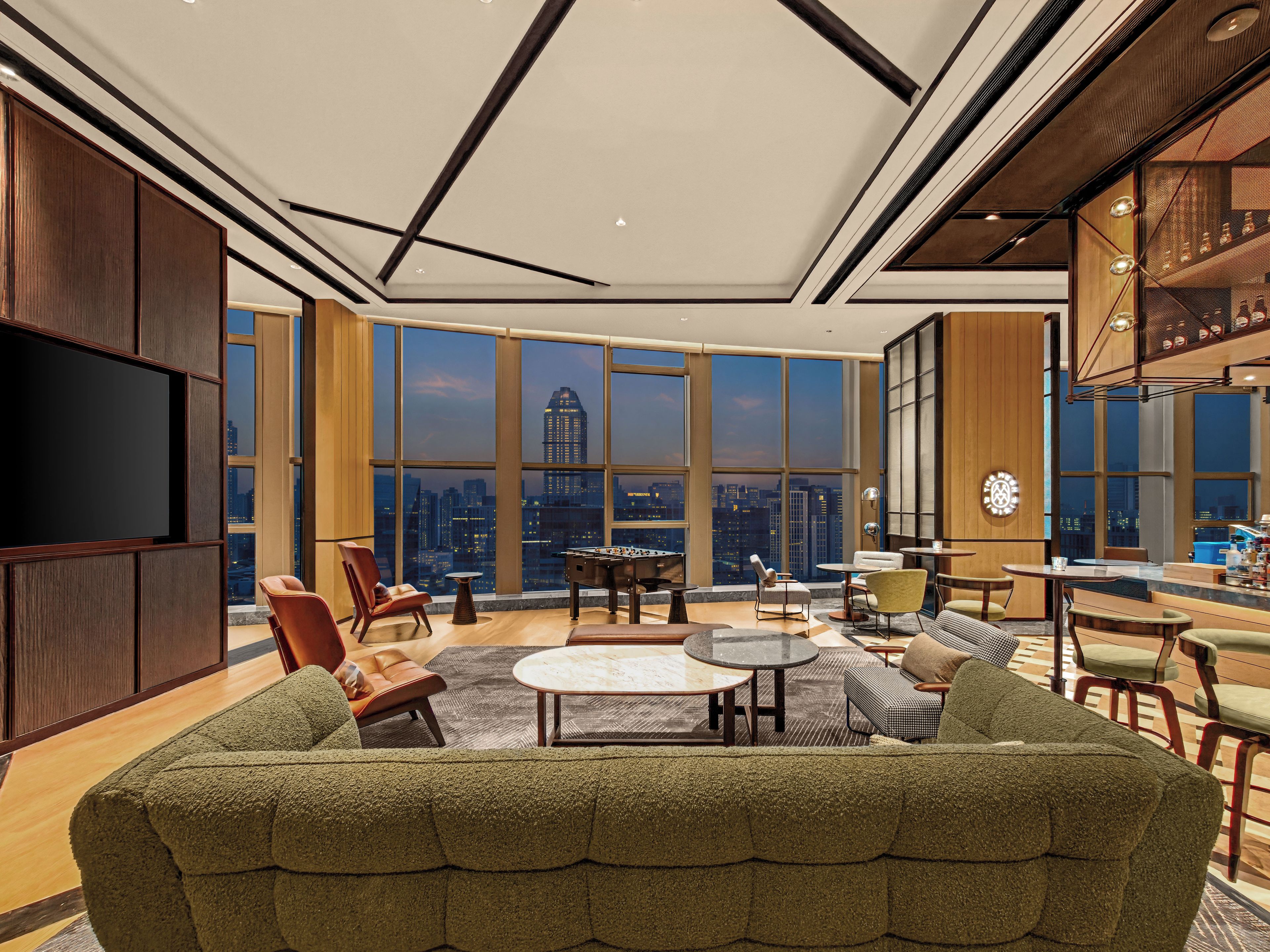A spacious living area with a large sofa, a coffee table, and a city view through expansive windows.