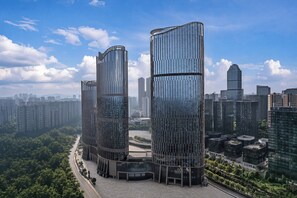 A modern high-rise building with a curved glass facade, surrounded by a dense urban skyline and a river.