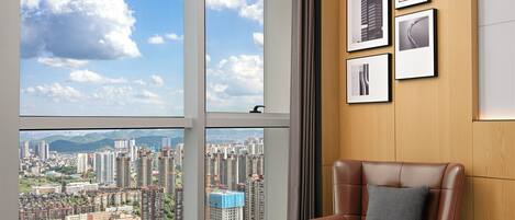 A hotel room with a large window, a brown leather chair, a small round table, and framed pictures on the wall.