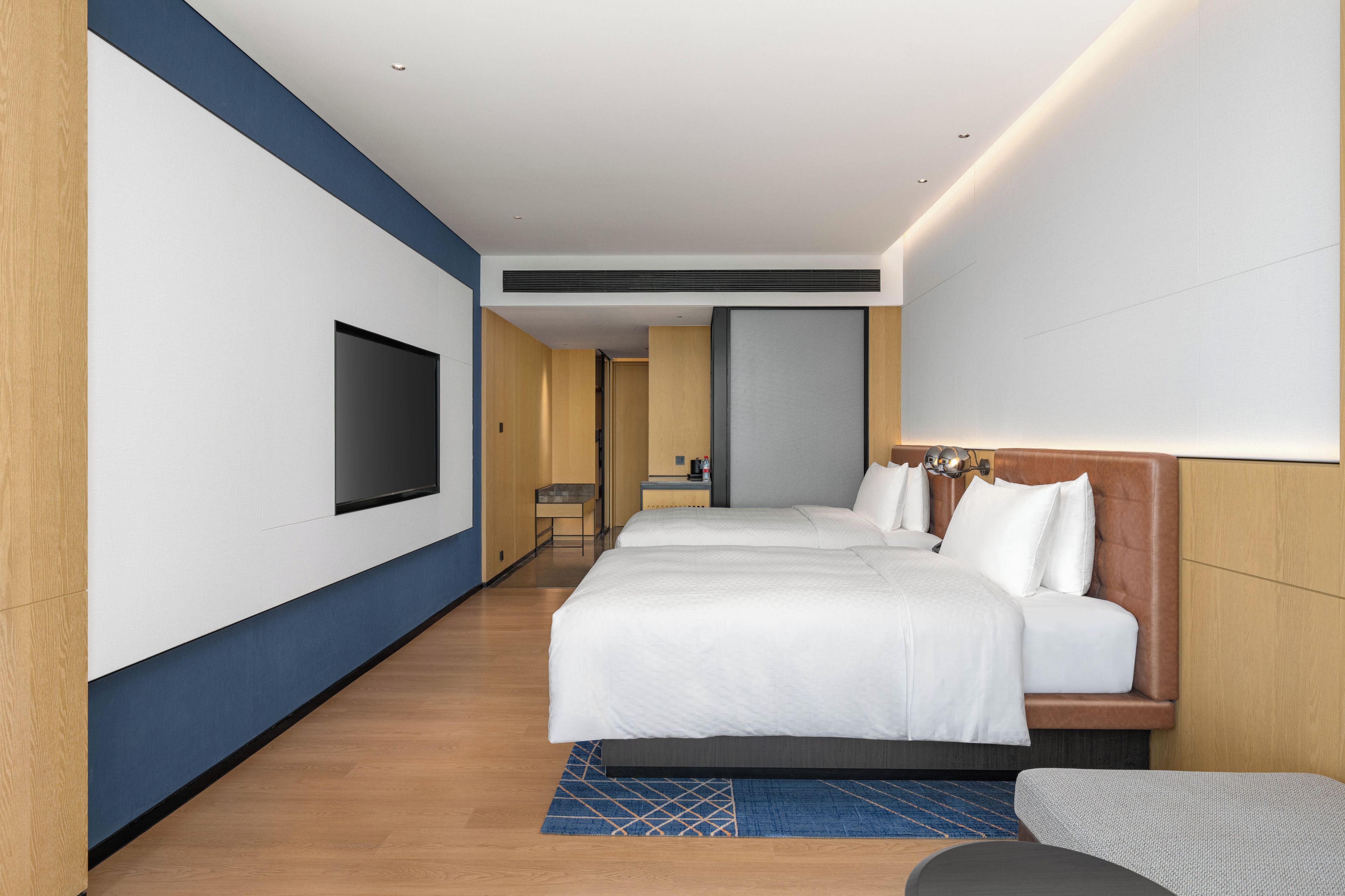 A hotel room with a large bed, a TV mounted on the wall, and a small desk with a chair.