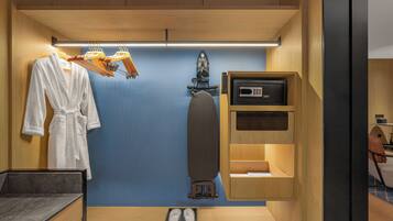 A compact hotel room with a built-in ironing station, a small seating area, and a robe drying rack.