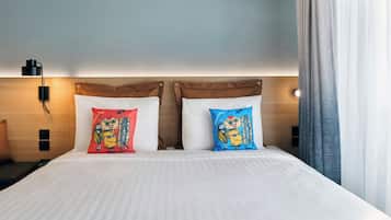 A hotel room with a bed, two pillows with cartoon characters, a nightstand, a lamp, and a window with curtains.