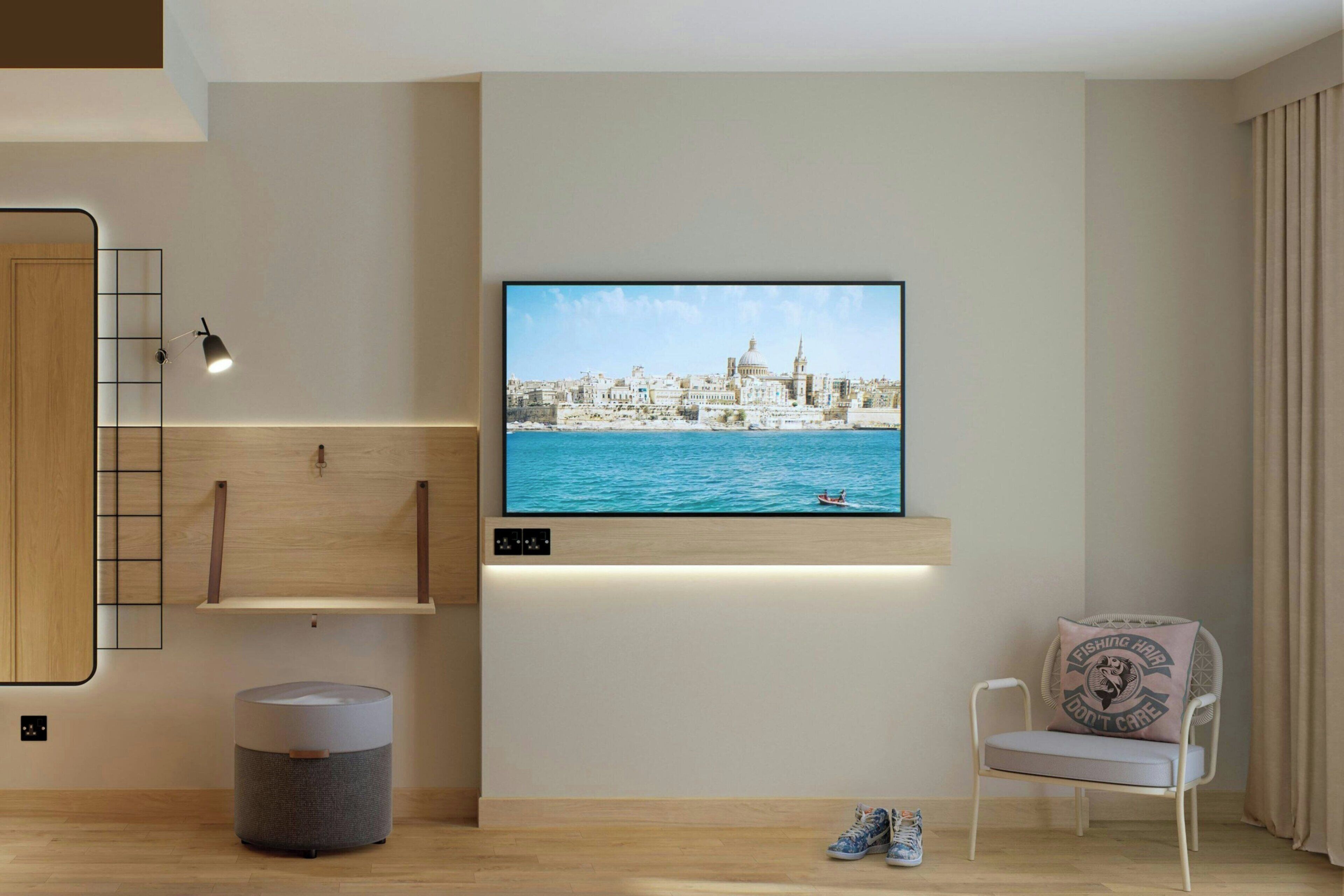 Een moderne woonkamer met een flatscreen televisie aan de muur, een houten vloer, een rond poefje, een witte stoel met kussen en een kleine tafel.