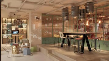 Un interior moderno con comedor que incluye una mesa de madera y taburetes de bar, rodeado de estanterías con objetos decorativos y una pared con dibujos técnicos.