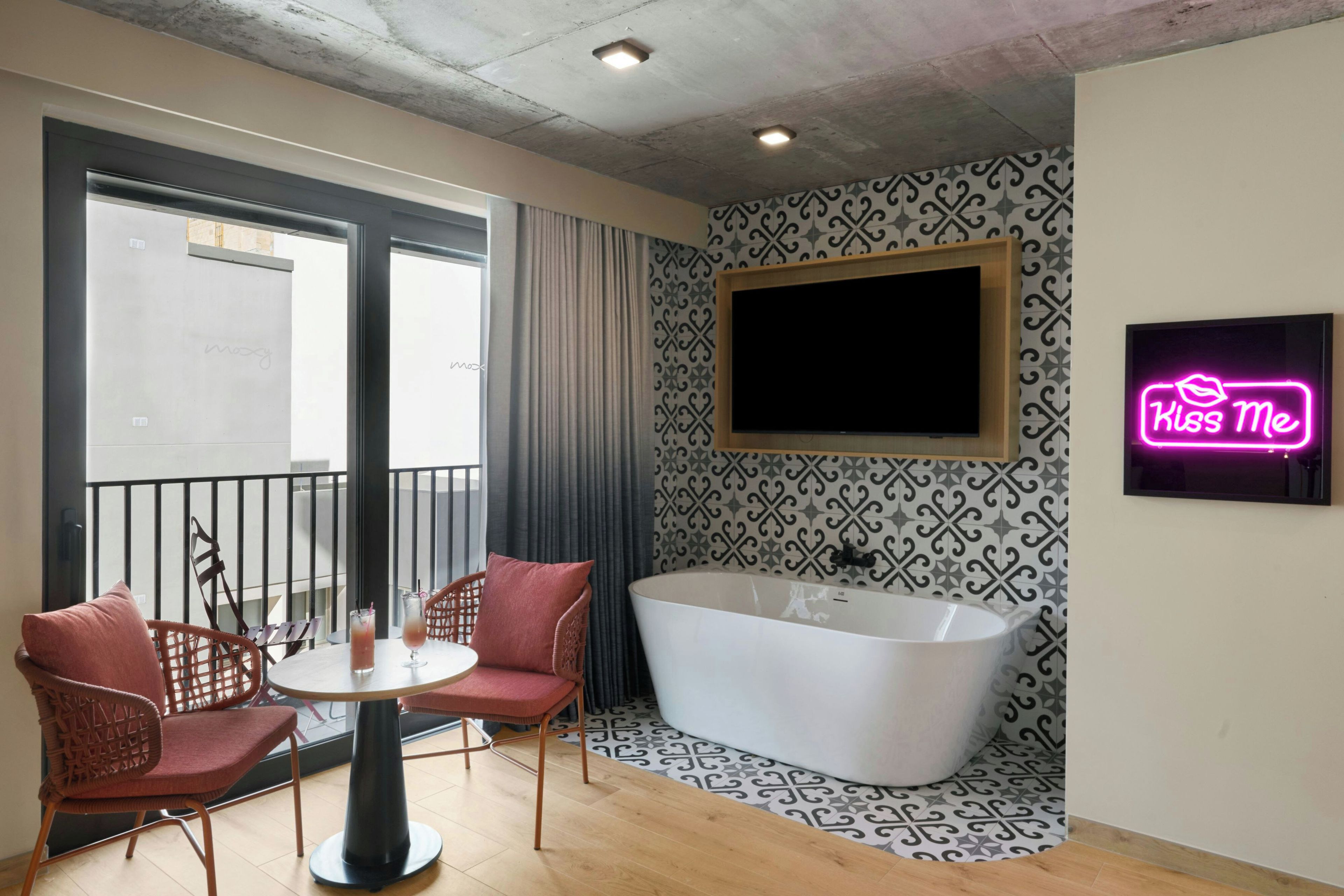 Un baño moderno con una bañera independiente, una mesa redonda con dos sillas y un letrero de neón.