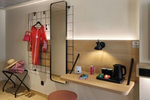 Una habitación pequeña con un escritorio de madera, un zapatero colgante, un taburete y un espejo.