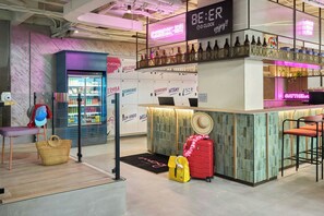 Zona de bar con letrero de neón, un refrigerador con bebidas y un área de descanso con un sombrero y equipaje.