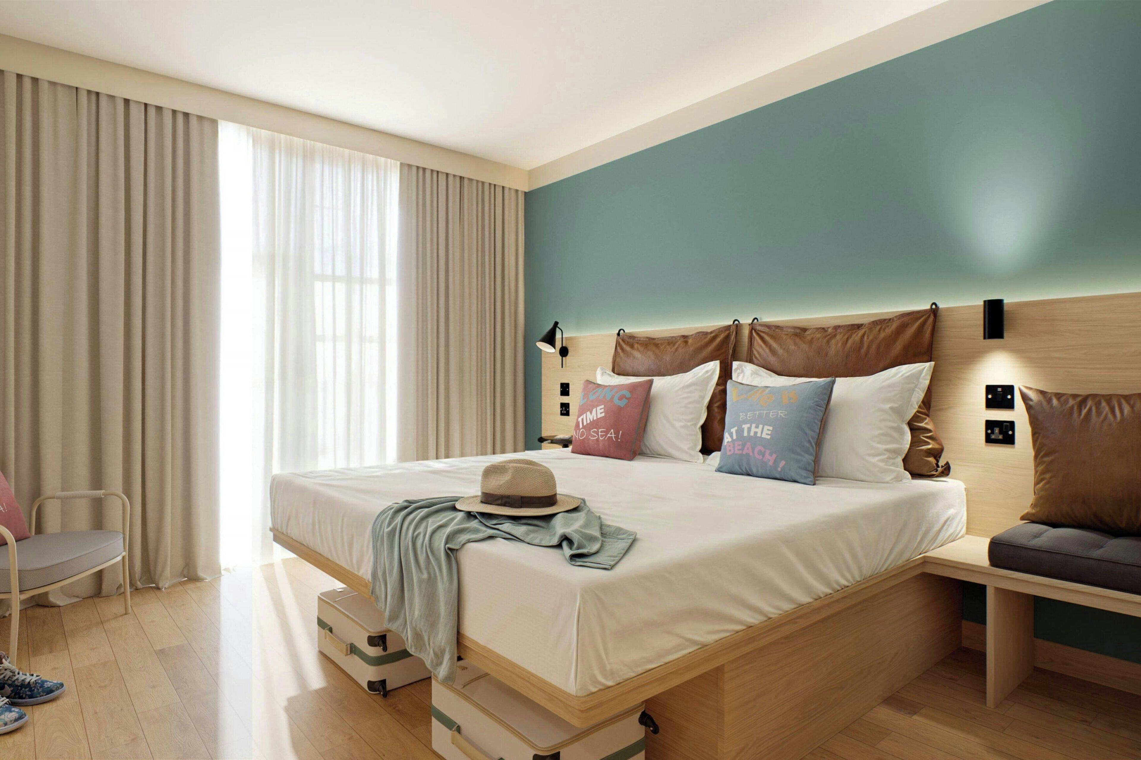 Habitación de hotel ordenada con una cama, mesitas de noche, una maleta y una silla.