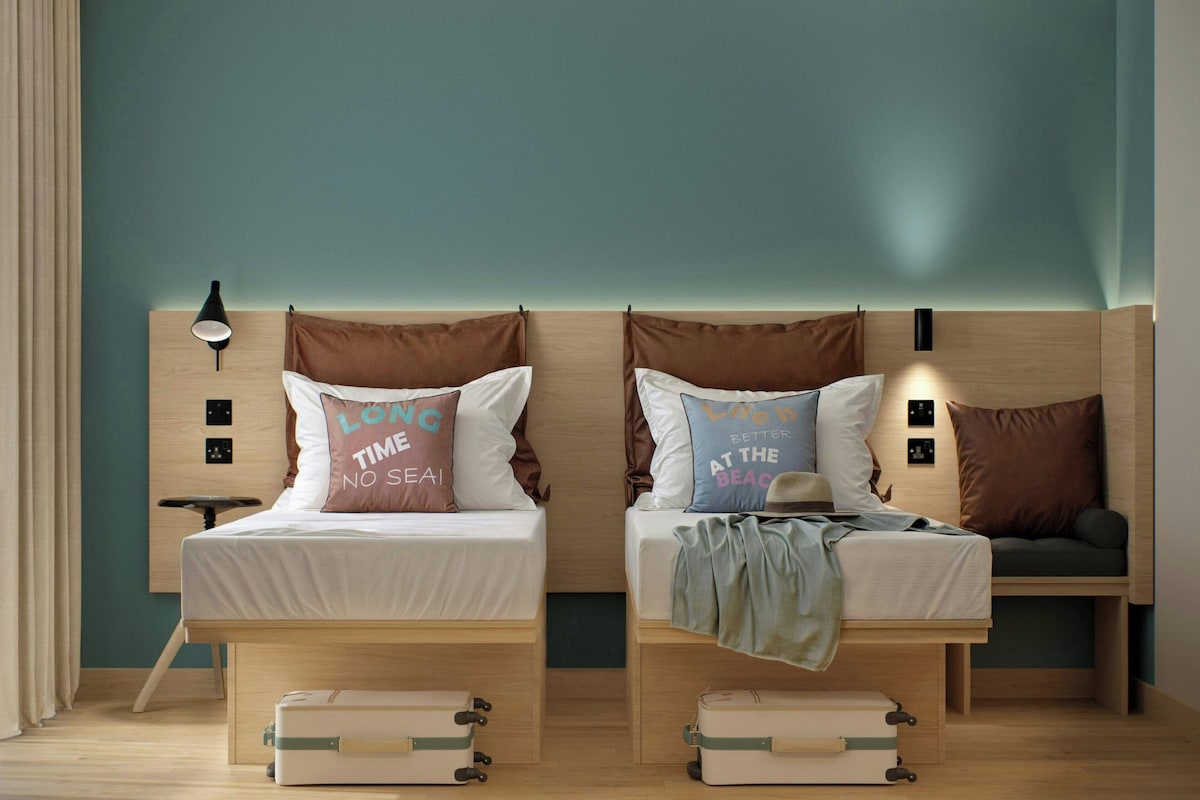 A twin room with two beds, each with a pillow featuring a travel-related message.