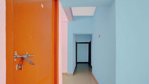 Ein Flur mit einer geschlossenen, orangefarbenen Tür, einer blauen Wand und einem gefliesten Boden.