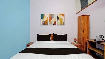 Una habitación de hotel con una cama, un armario de madera, una mesita de noche y tres cuadros abstractos en la pared.