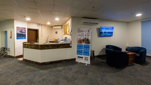 Un espace d’accueil doté d’un comptoir en marbre, d’une horloge et d’un écran numérique affichant des informations.