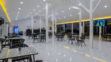 A spacious indoor area with multiple tables and chairs, a vending machine, and a television screen mounted on the wall.