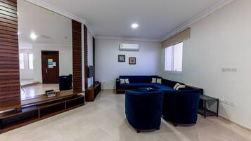 A living room with a dark blue sofa set, a wooden entertainment unit, and a large mirror.