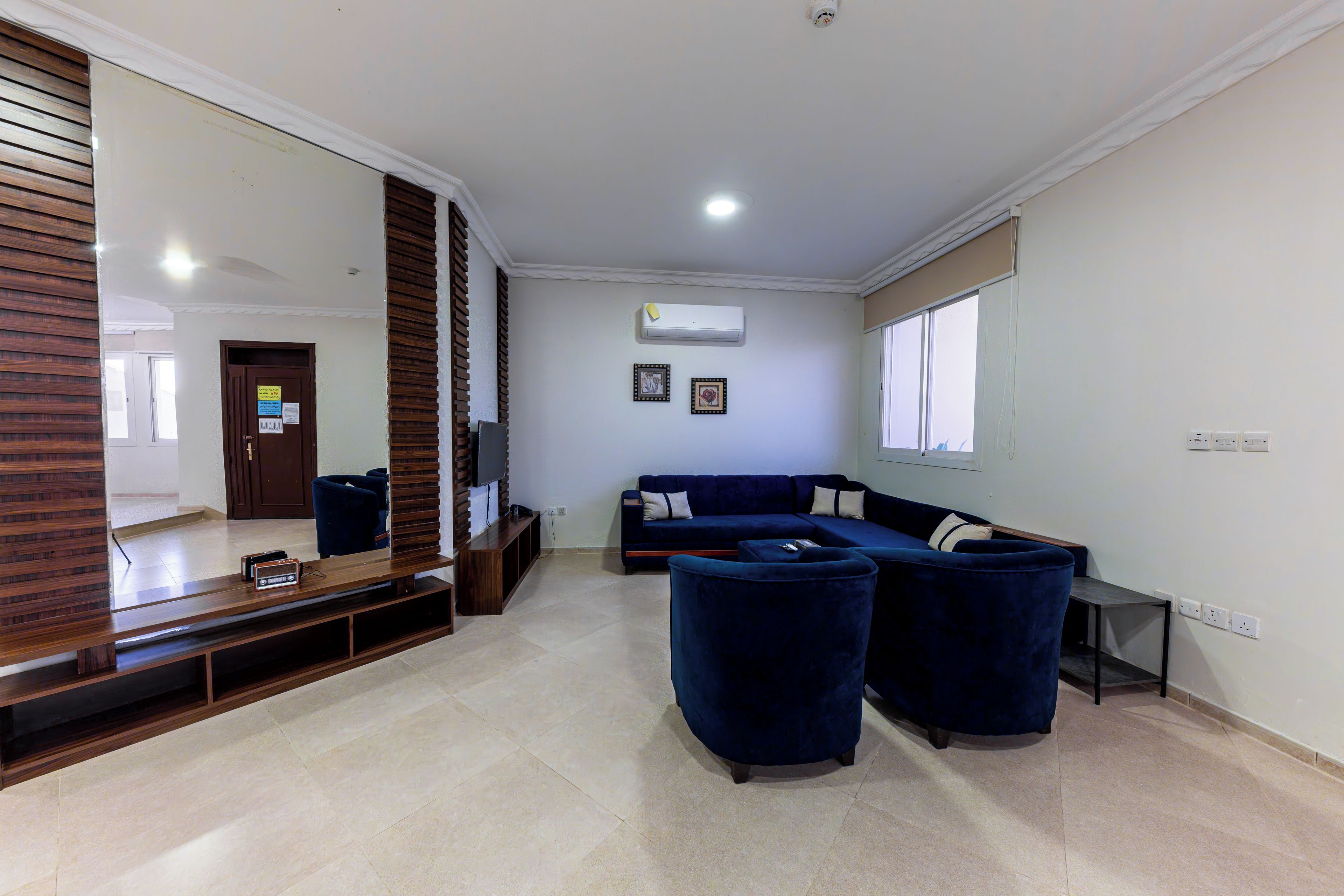 A living room with a sectional sofa, a TV on a wooden stand, and a large mirror.