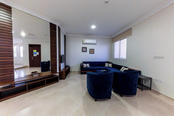 A living room with a sectional sofa, a TV on a wooden stand, and a large mirror.