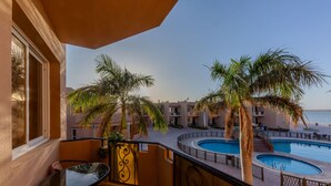 Un balcón con vista a una piscina y palmeras, una mesa de vidrio y una silla.