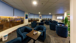 Un espace lounge moderne doté de sièges confortables, d’un bar à café et d’une grande fenêtre offrant une vue sur la ville.