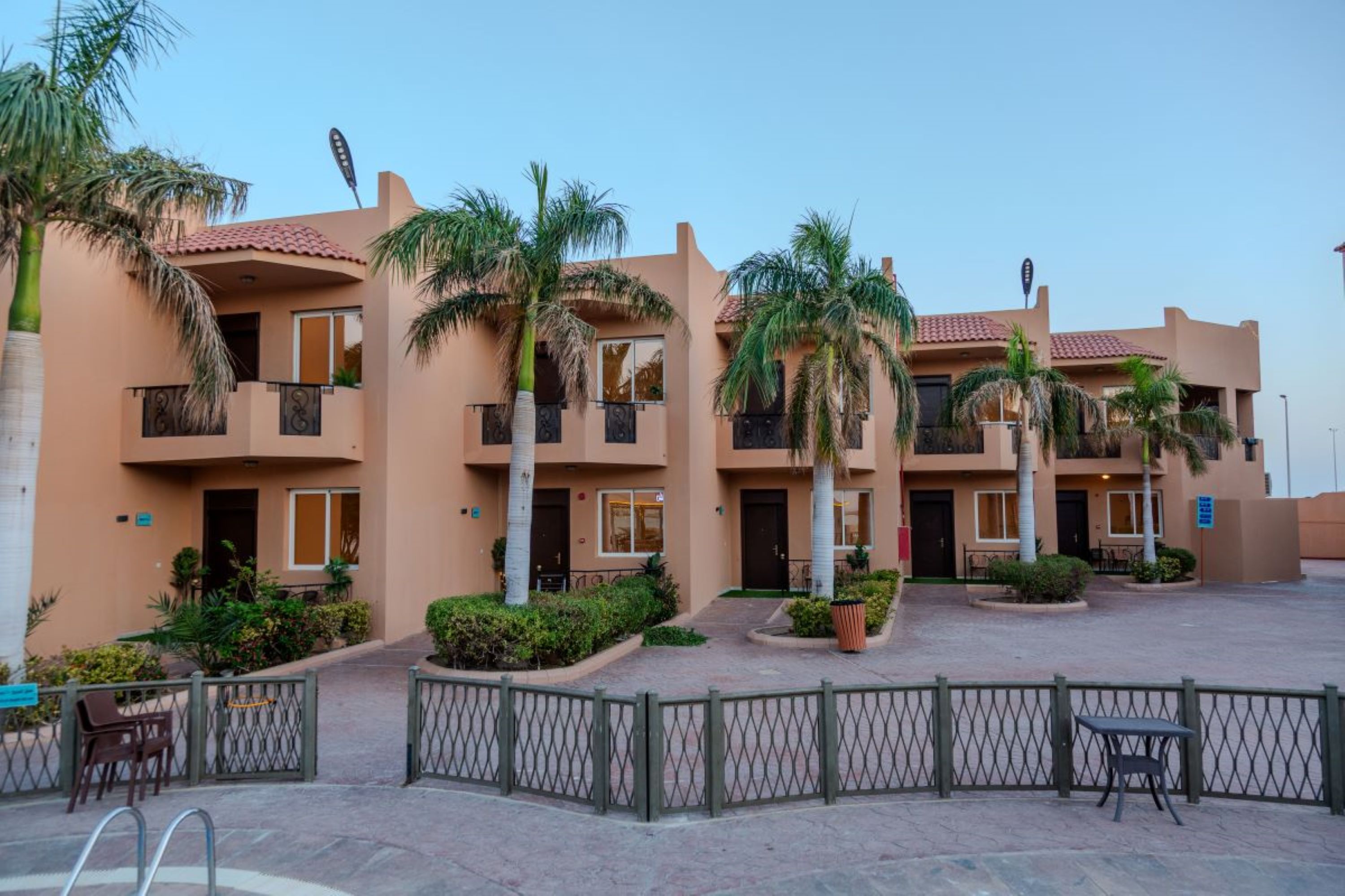 A multi-story hotel with balconies, palm trees, and a paved courtyard.