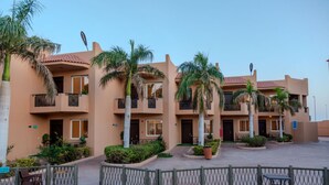 Un hotel de varios pisos con balcones, palmeras y un patio empedrado.