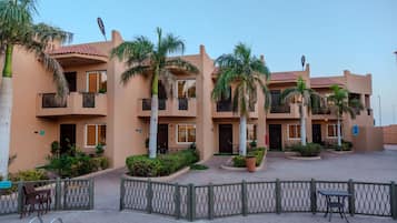 A multi-story hotel with balconies, palm trees, and a paved courtyard.