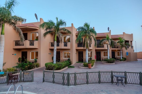 Un hotel de varios pisos con balcones, palmeras y un patio empedrado.