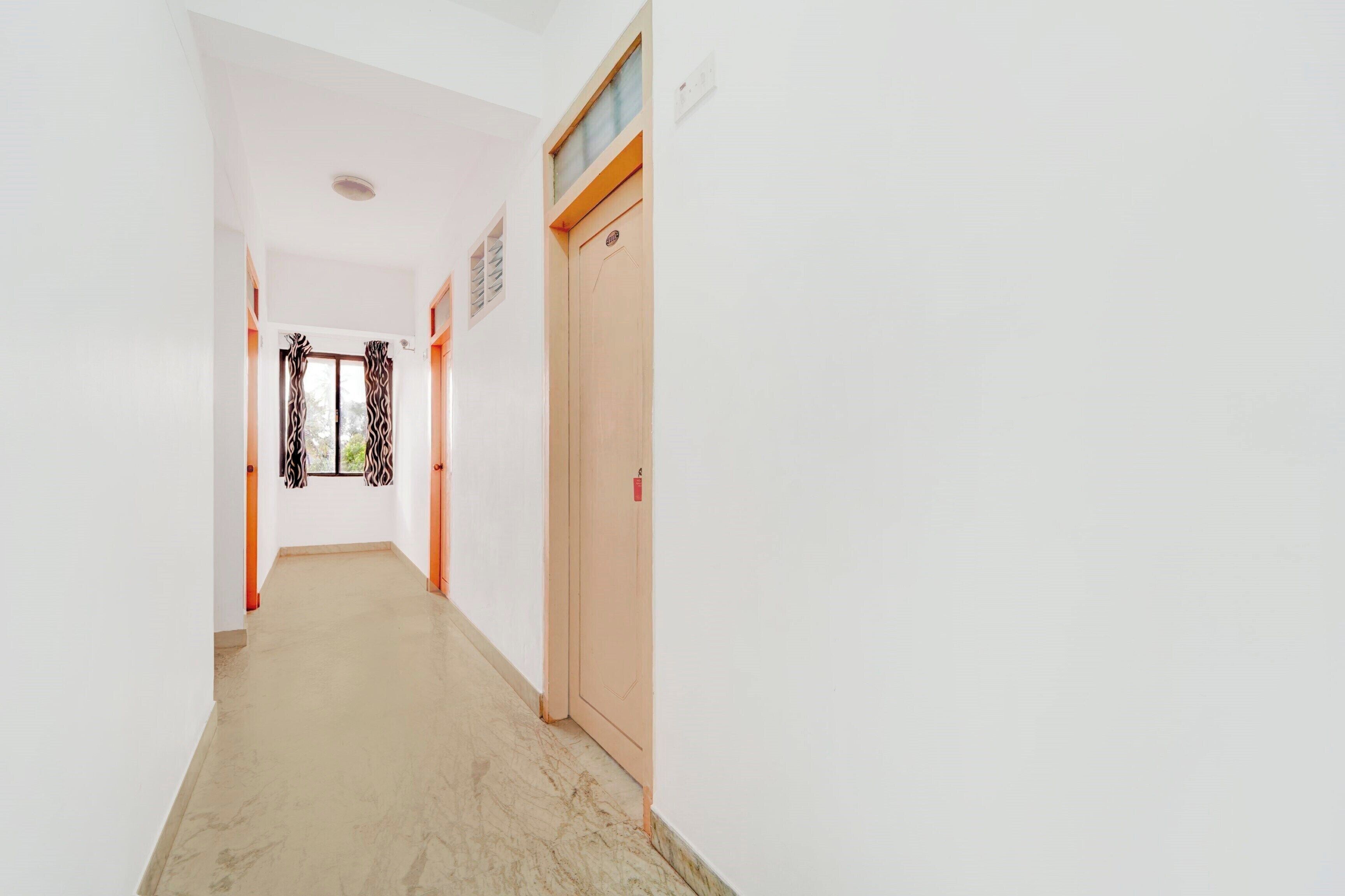 A corridor with a door on the right, a window with curtains, and a ceiling light fixture.