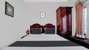 A hotel room with a large bed, a wooden wardrobe, a framed picture on the wall, and a window with curtains.