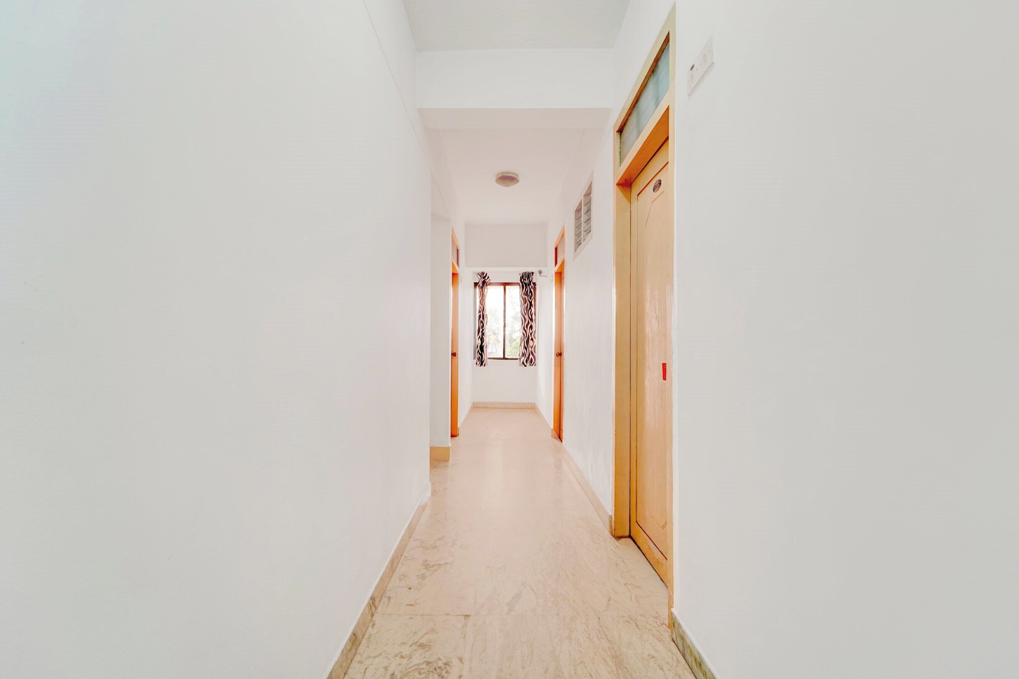 A corridor with a door at the end, a light switch on the wall, and a patterned curtain.