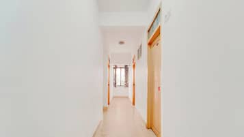 A corridor with a door at the end, a light switch on the wall, and a patterned curtain.