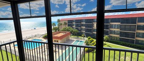A balcony with a view of a beach, a pool, and a building with a red roof.