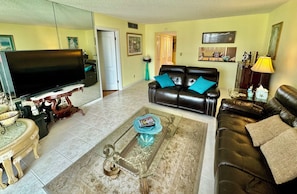 A living room with a flat-screen TV, leather sofas, a coffee table, and a dining table with chairs. - Beachfront Condo (Redington Shores)