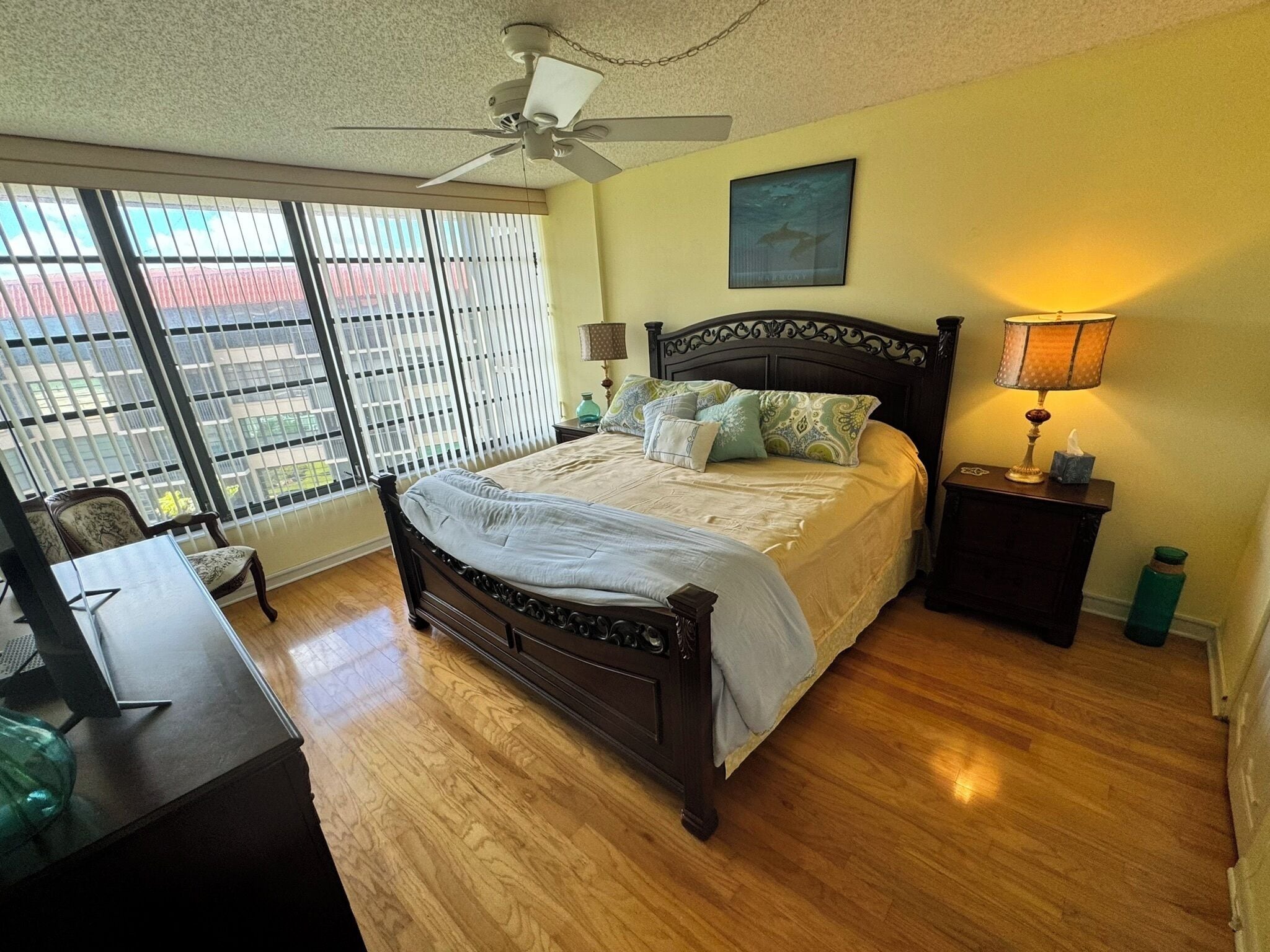 A bedroom with a bed, a desk, a chair, a lamp, and a window with blinds.
