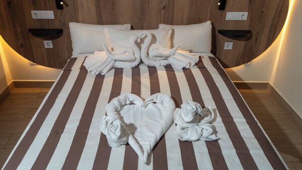 Habitación de hotel con colcha a rayas, toallas dispuestas en forma de corazón y cabecera de madera.