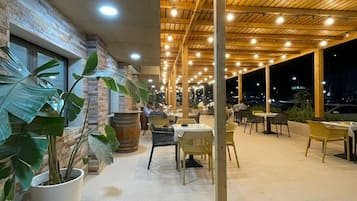 Un espacio de comedor al aire libre con mesas y sillas, un muro de ladrillo y plantas en macetas.
