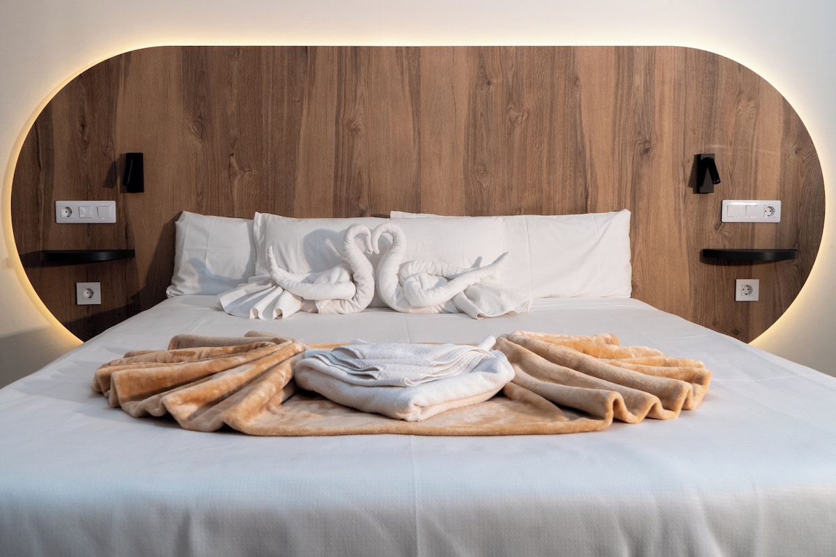 Un lit bien fait, avec du linge de lit blanc, une tête de lit en bois et deux interrupteurs fixés au mur.