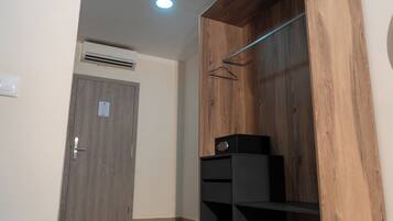 A room with a wooden wardrobe, a door with a handle, a hanging coat rack, and a small black speaker on a shelf.