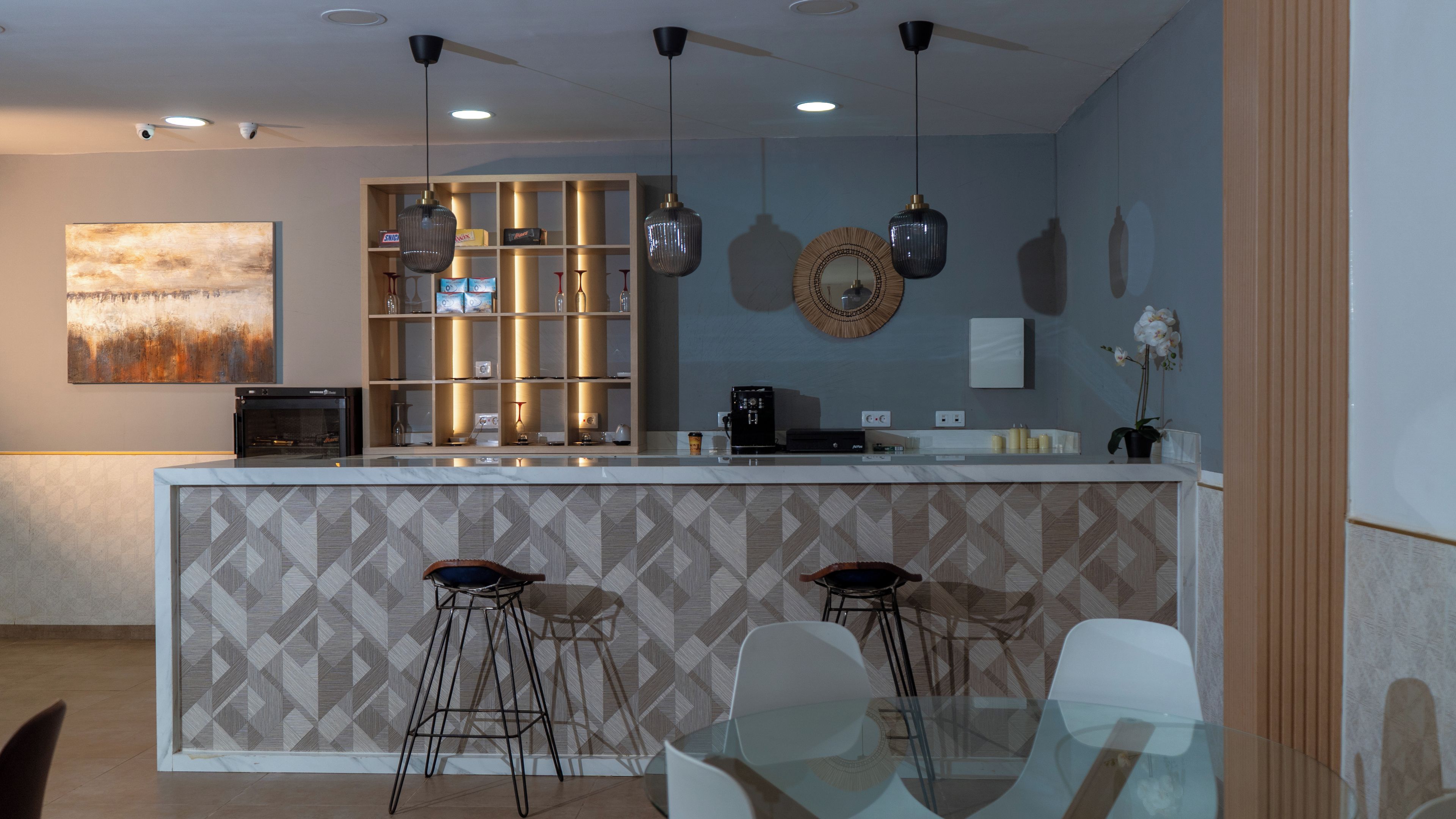 Una cocina moderna con una isla central, taburetes de bar, iluminación colgante y un adorno en la pared.
