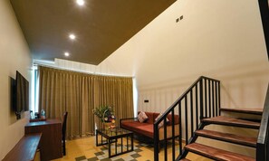 Un salón con sofá, una mesa de centro, un televisor en la pared y una escalera.