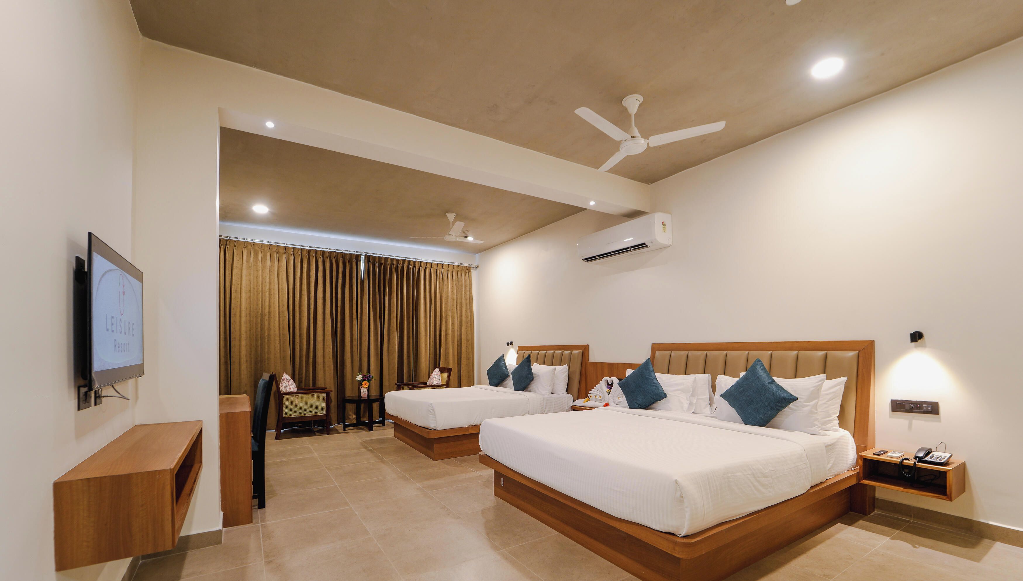 A hotel room with two beds, a TV, a ceiling fan, an air conditioning unit, and a small table with a phone.