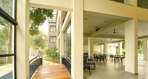 Un espacio al aire libre techado con mesas y sillas, un paseo de madera y vistas a un edificio con ventanas.