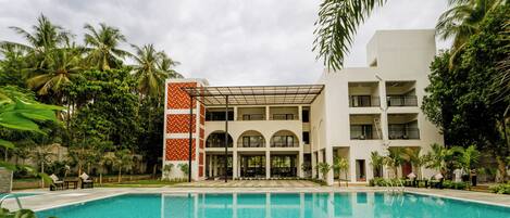 Un hotel con piscina, varios balcones y abundante vegetación.