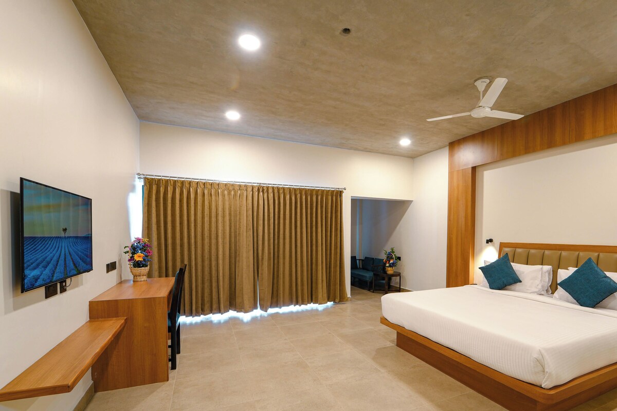 Habitación de hotel con cama, mesita de noche, escritorio con silla, televisor y ventana con cortinas.