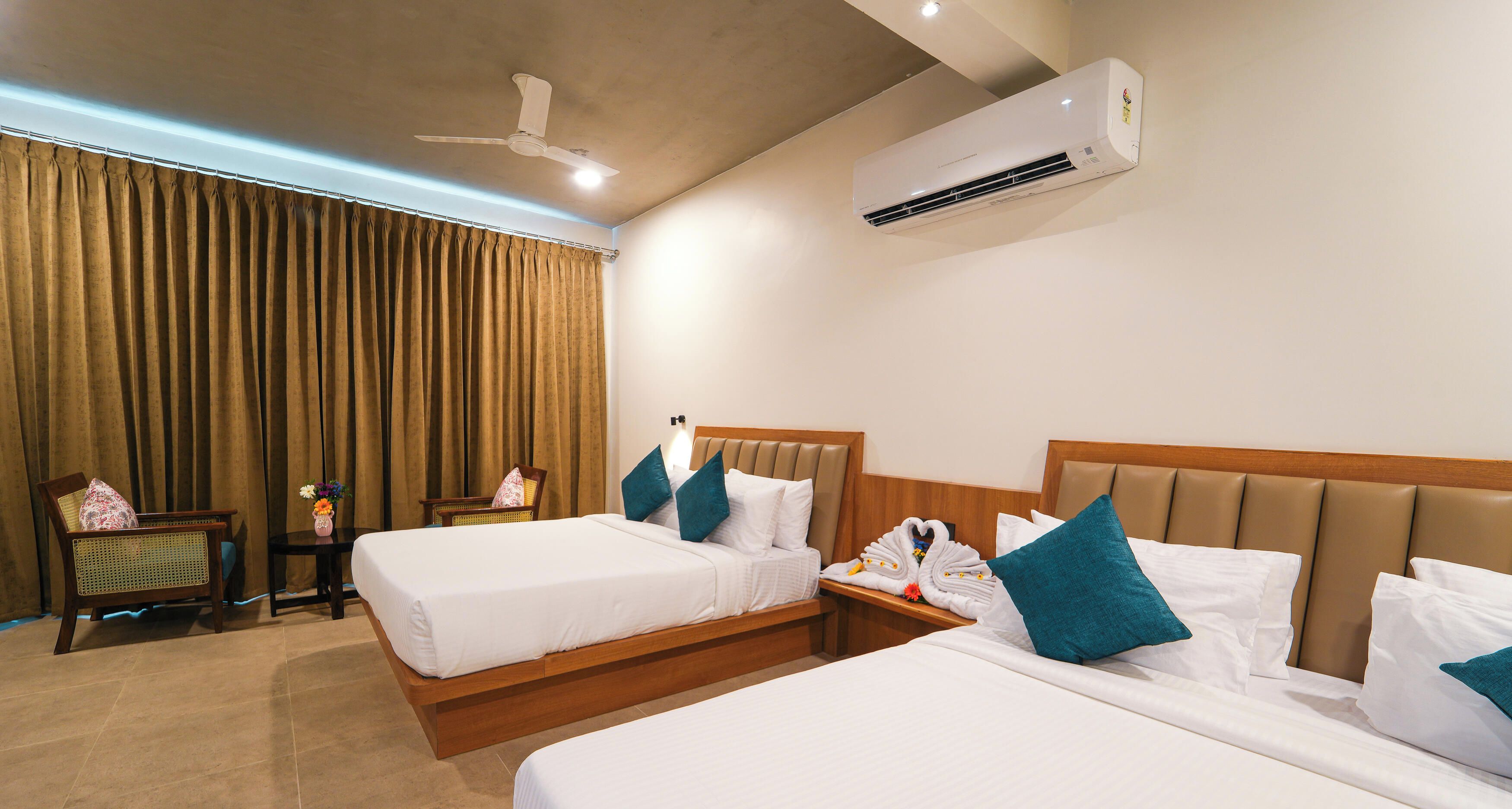 Een hotelkamer met twee bedden, een plafondventilator, een airconditioning en een raam met gordijnen.