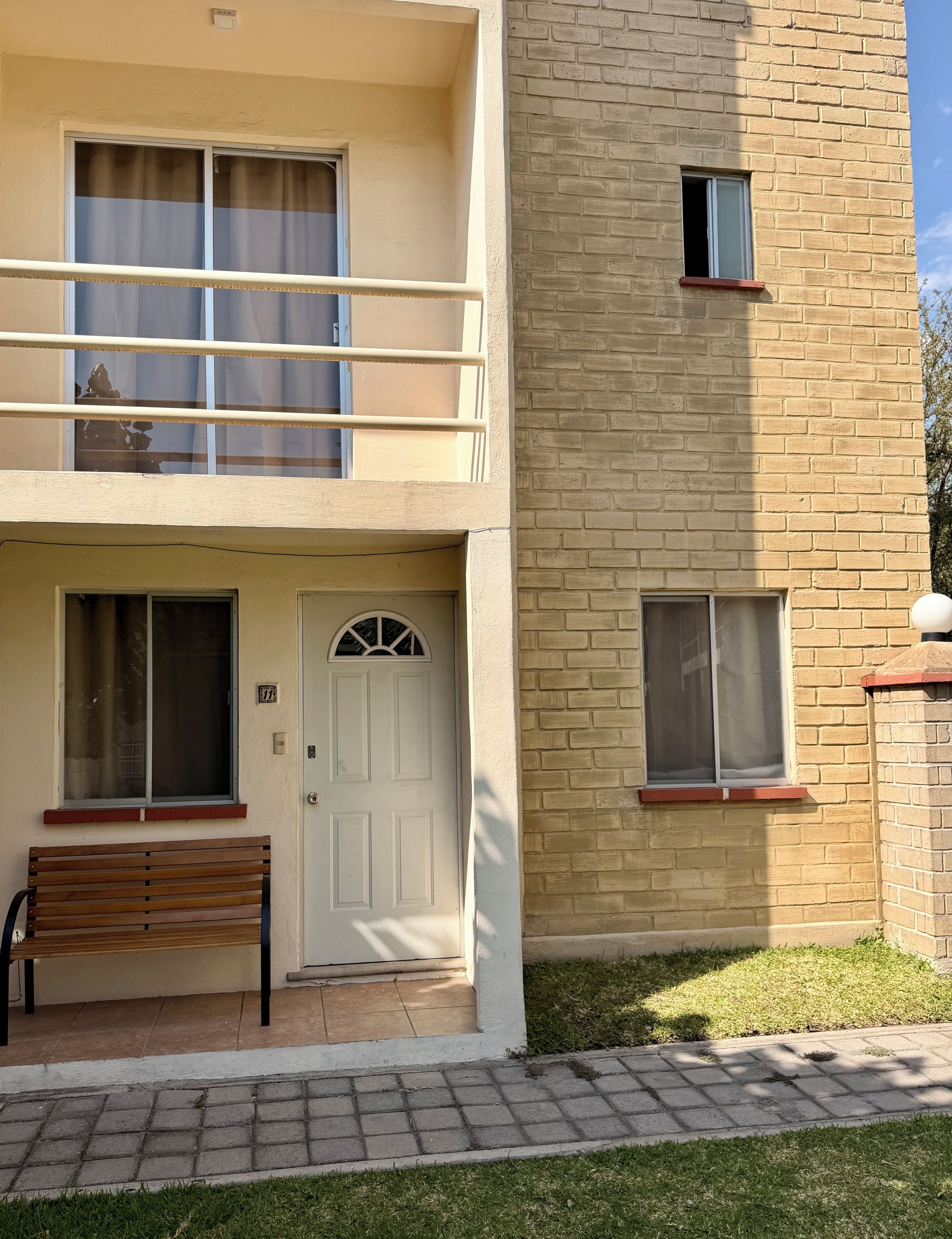 Un bâtiment à deux étages, avec une porte d’entrée, un banc et une petite fenêtre.
