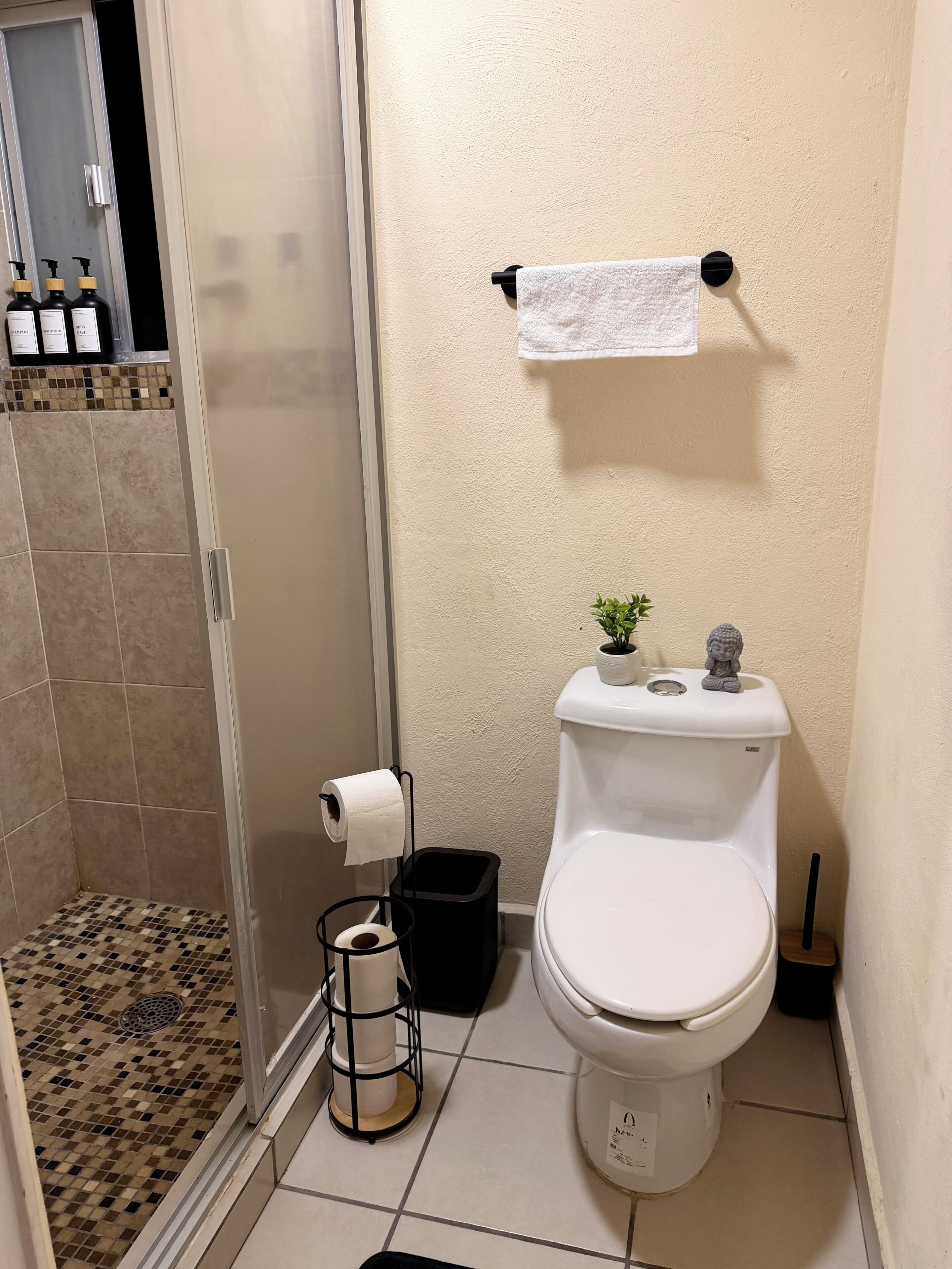 Et badeværelse med toilet, bruser, håndklædeholder og skraldespand.