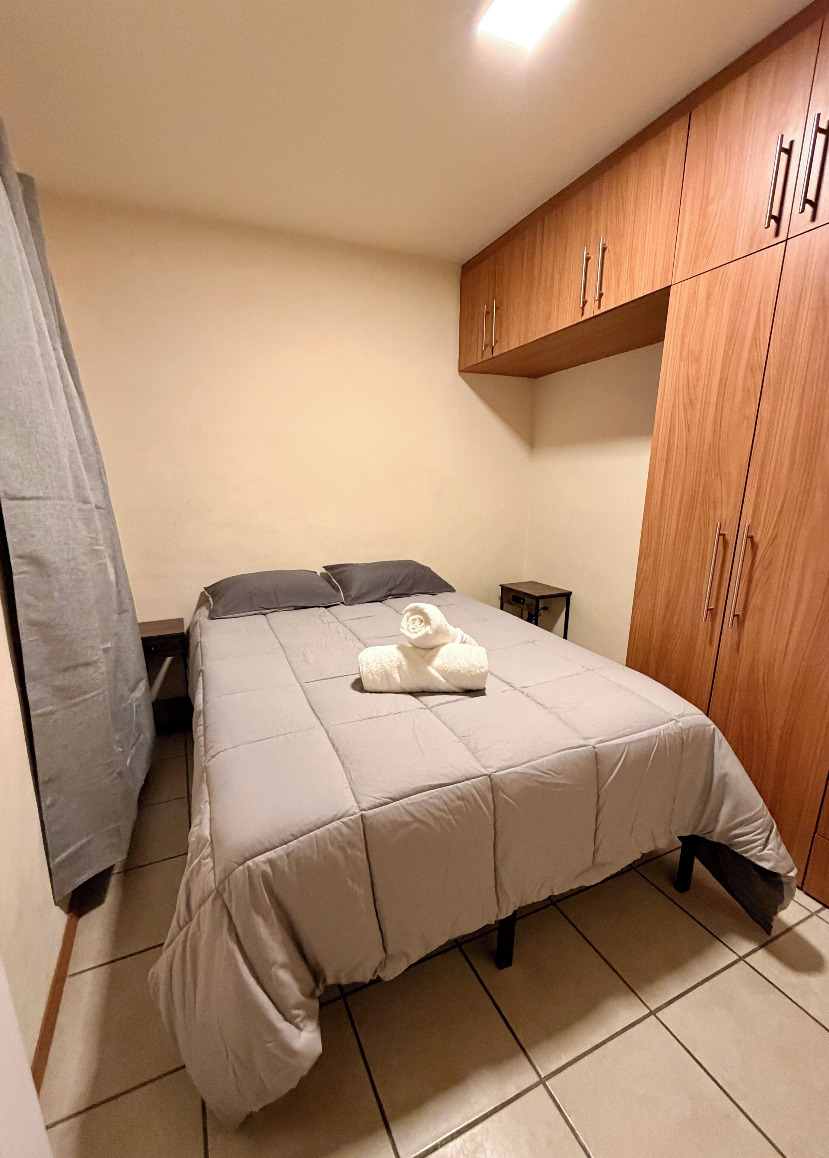 A bedroom with a bed, a wooden wardrobe, a nightstand, and a towel on the bed.