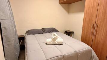 A bedroom with a bed, a wooden wardrobe, a nightstand, and a towel on the bed.